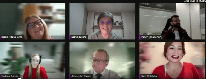 Se observa una videollamada de zoom con seis cámaras. La primera es la de una mujer de mediana edad rubia con gafas negras. A su derecha una mujer de la misma edad con gafas transparentes y el pelo gris corto. Después un hombre joven con el pelo y barba engra y gafas. Debajo, la cámara de una mujer joven con el pelo corto castaño claro, jersey rojo y labios del mismo color. A su izquierda un señor mayor con el pelo cano, gafas, una blusa blanca y una corbata negra. Por último a su izquierda una muchacha joven rubia con el pelo muy largo y una blusa roja.