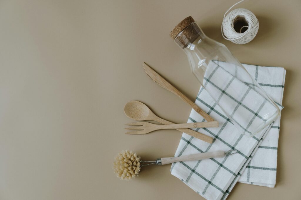 Flat lay of eco-friendly kitchen utensils including a glass jar and wooden cutlery on a checkered napkin.