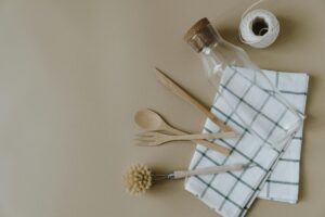Flat lay of eco-friendly kitchen utensils including a glass jar and wooden cutlery on a checkered napkin.